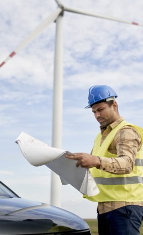 Latin male engineer standing on wind turbine field and checking paper project